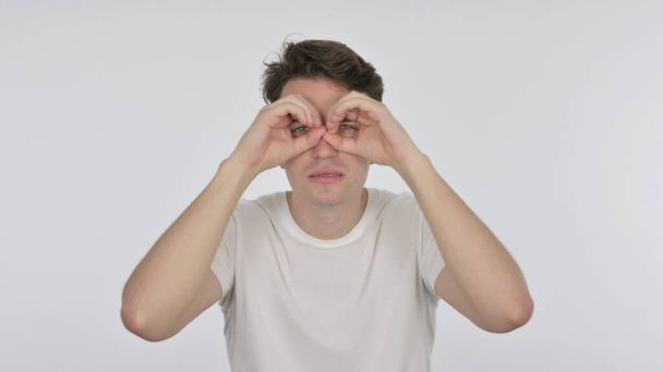 Buscando Hombre joven casual con gesto binocular sobre fondo blanco - Foto, Imagen