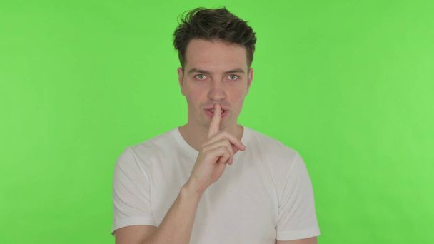 Schweigen Sie bitte, lässiger junger Mann mit Finger auf Lippen auf grünem Hintergrund - Foto, Bild