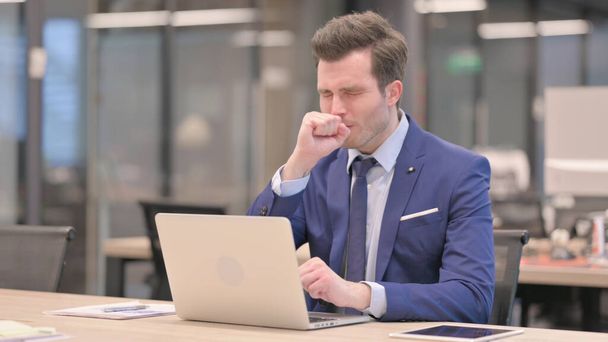 Empresario de mediana edad tosiendo mientras usa el ordenador portátil en la oficina - Foto, imagen