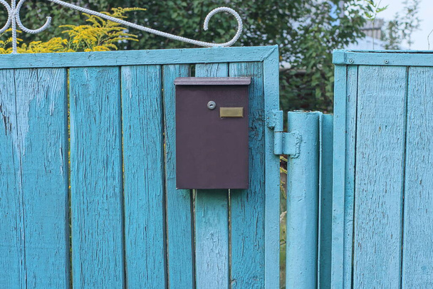 one brown metal mailbox hanging on a blue wooden fence wall on a rural street - Zdjęcie, obraz