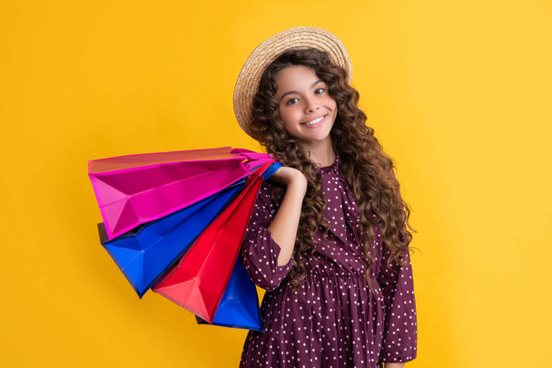 happy child with curly hair hold shopping bags on yellow background. - Foto, immagini