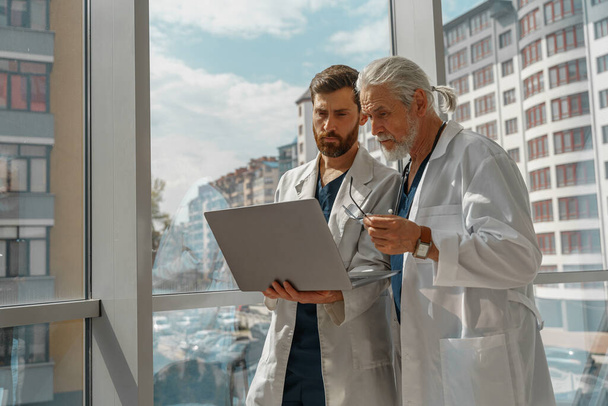 Δύο γιατροί συνάδελφοι συζητούν ασθενή στάση διάγνωση στην ιατρική κλινική κοντά σε πανοραμικά παράθυρα - Φωτογραφία, εικόνα