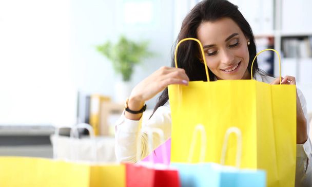 Beautiful woman is amazed to see gift in shopping bag. Concept of shopping and gifts - Fotó, kép