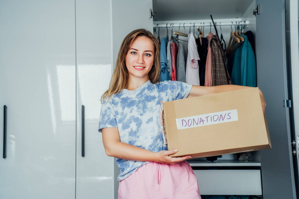 Smiling Woman with box of selected clothes from her wardrobe for donating to a Charity. Decluttering, Sorting clothes And Cleaning Up. Reuse, second-hand concept. Conscious consumer, sustainability. - Foto, imagen
