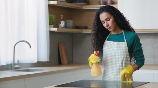 Female house cleaner pretty young mother housewife maid wears apron yellow rubber gloves splash detergent antibacterial spray on electric oven wash kitchen furniture stove by wet rag domestic chores - Felvétel, videó