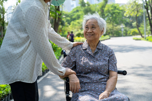 Bakıcı yardım ve bakım Asyalı yaşlı ya da yaşlı kadın hasta parkta tekerlekli sandalyede oturuyor, sağlıklı güçlü tıbbi konsept. - Fotoğraf, Görsel
