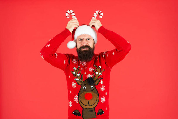confused brutal hipster man in santa hat with party decoration on red background, new year. - Foto, imagen