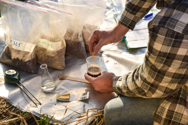 Male agronomy specialist testing soil sample outdoors, using laboratory equipment, performing soil certification at agricultural grain field sunrise. Environment research, soil certification - Foto, immagini