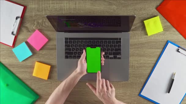 The coder is showing the programming courses on the phone green screen mockup concept. Vertical position. Workplace with laptop, color stickers, files. - Filmagem, Vídeo