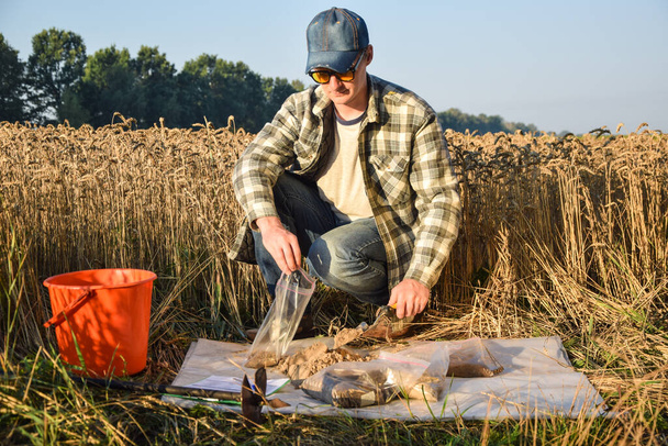 Closeup of agronomy specialist preparing soil samples for laboratory analysis outdoors. Professional farmer filling sample bag with material sampling at field. Environment research, soil certification - Foto, imagen
