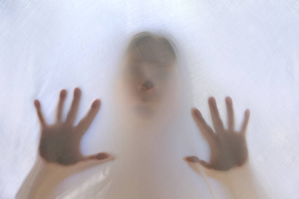 eerie blurry hands and face of girl, victim of violence behind window, dense fabric, wrap, ghost, spirit trying to reach out from afterlife, concept of friday 13th, nightmares, halloween horror - Fotografie, Obrázek