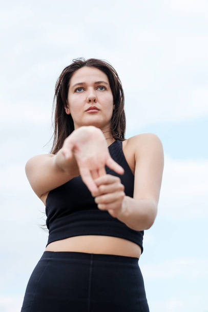 Портрет молодої білої жінки-йоги, що розтягує руки. Вона дивиться геть, і вона носить чорний бак зверху
. - Фото, зображення