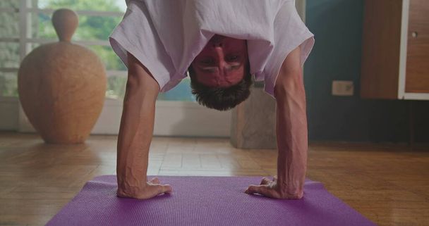 Athlete man balances upside down in yoga practice. Person practicing balance position indoor at living room home. Man doing handstand - Photo, Image