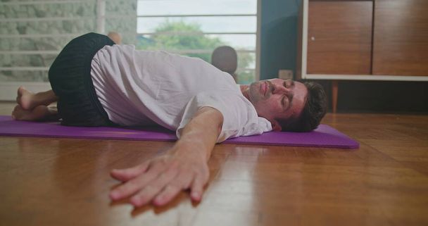Man stretches on a mat in the living room and practices yoga. He does flexibility exercises and keeps himself fit and healthy. - Foto, afbeelding
