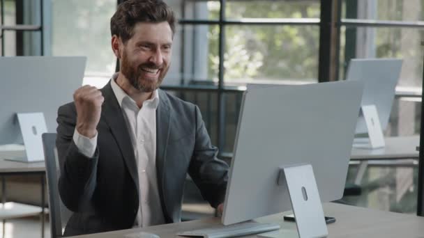 Щасливий кавказький бородатий бізнесмен в офісі, який дивиться на екран комп'ютера з ентузіазмом переможець радіє онлайн виграшем Фінансові ставки зростання Людина-директор працівник з радістю відзначає успіх - Кадри, відео