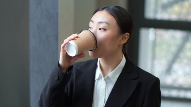 Coffee break at office. Close up portrait of young pensive asian woman employee drinking takeout coffee, looking aside at window, free space, slow motion - Felvétel, videó