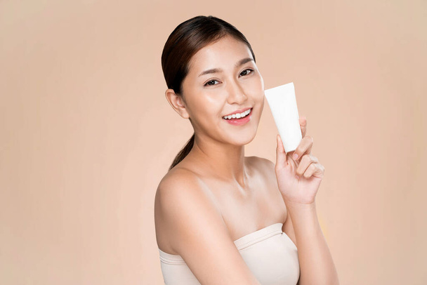 Жінка, яка посміхається, тримає макетний продукт для рекламного текстового місця, світло-сірого фону. Концепція охорони здоров'я для шкіри, косметичний засіб для реклами
. - Фото, зображення