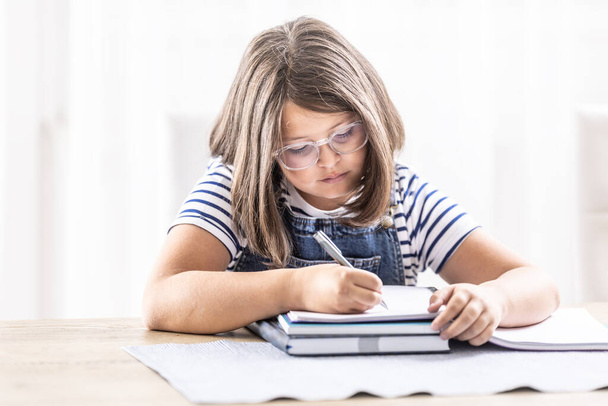 Bored girl writes homework into an exercise book. - Foto, imagen