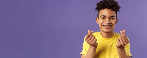 Close-up portrait of lovely cute young man with afro haircut, showing korean heart finger signs and smiling, express his love and sympathy towards person, stand purple background. - Valokuva, kuva