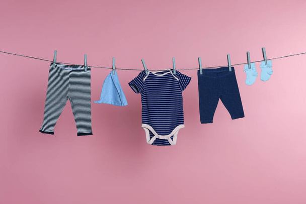 Different baby clothes drying on laundry line against pink background - Foto, Bild