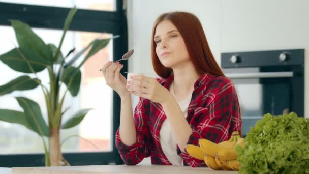 Vegetarian caucasian woman redhead female vegan girl sit in kitchen eat dairy creamy desert on breakfast healthful morning snack yogurt with minimal calorie keep diet taste delicious brunch bodycare - 映像、動画