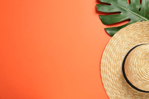 Stylish straw hat and tropical leaf on orange background, flat lay. Space for text - Foto, imagen