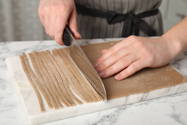 Woman making soba (buckwheat noodles) with knife at white marble table indoors, closeup - Фото, зображення