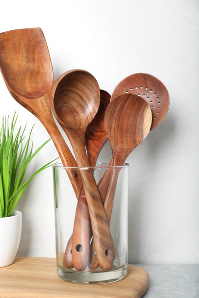 Set of wooden kitchen utensils in glass holder and houseplant on light grey marble table - Photo, Image