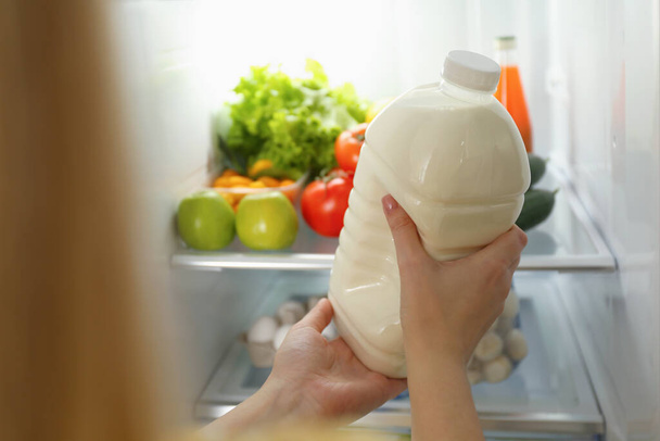 Young woman putting gallon of milk into refrigerator indoors, closeup - Foto, afbeelding