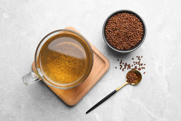 Cup of aromatic buckwheat tea and granules on light marble table, flat lay - Foto, imagen