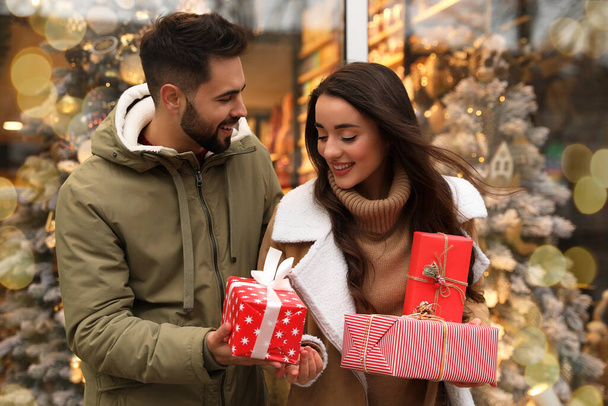 Lovely couple with presents near store decorated for Christmas outdoors - Φωτογραφία, εικόνα