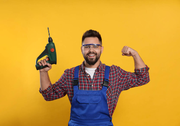 Young worker in uniform with power drill on yellow background - Фото, зображення