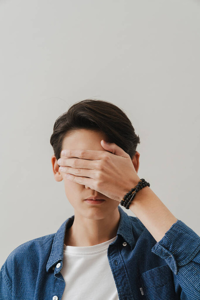 Asian boy wearing shirt covering his eyes while posing on camera isolated over white background - Фото, зображення