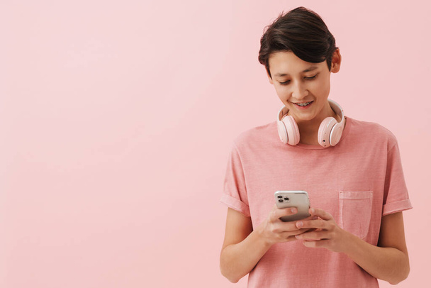 Asian boy wearing t-shirt smiling while using mobile phone isolated over pink background - Foto, Imagen