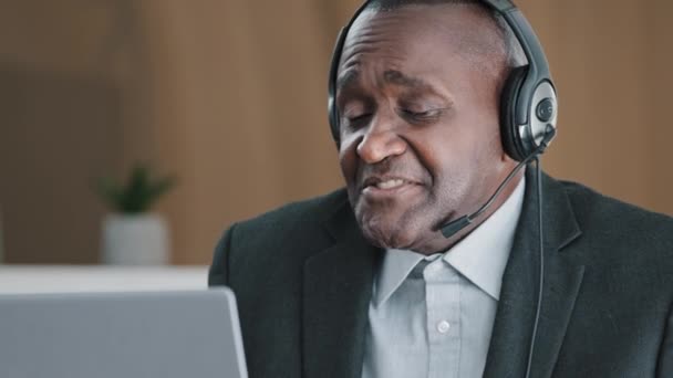 Elderly 50s African American man advisor operator male consultant remote teacher has online distant talk with client student chat video call conference wearing headset answer uncertain puzzled laugh - Πλάνα, βίντεο