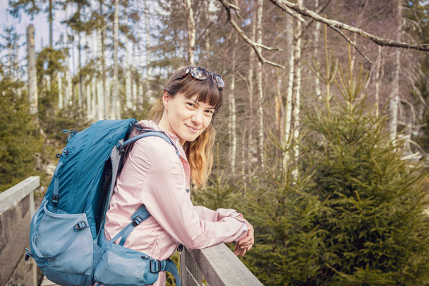 A young beautiful girl walks in the forest with a hiking backpack. Happy female traveler enjoying nature, looking at camera and smiling. - Foto, Bild