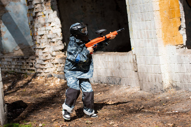a teenager with a machine gun and a paintball mask plays war - Foto, Imagen