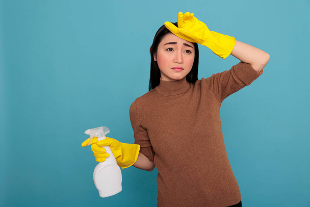 Young asian housewife stressed from daily work holding spray detergent in yellow rubber glove Cleaning home concept, Frustrated overwork housemaid with negative state of mind - 写真・画像