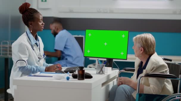 Specialist pointing at computer with greenscreen display at checkup with old woman in wheelchair. Medic and patient looking at chroma key background with isolated mockup copyspace. - Filmagem, Vídeo