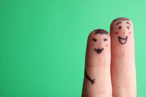 Two fingers with drawings of happy faces on green background, space for text. Spending time together - Фото, изображение