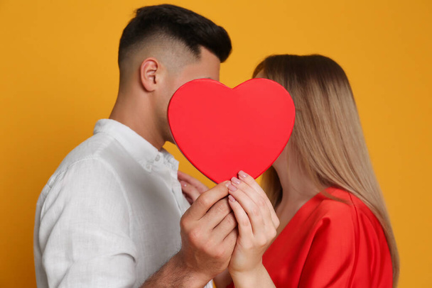 Lovely couple kissing behind decorative heart on yellow background. Valentine's day celebration - Fotografie, Obrázek