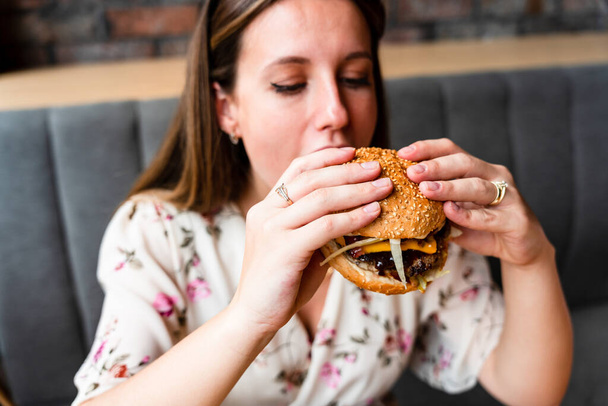 Woman hamburger eat. Hungry Caucasian Female Eating Tasty Burger. Fast food, people and unhealthy eating concept - Foto, imagen