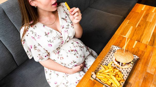 Pregnant woman hamburger eat. Hungry pretty pregnancy female eating tasty burger. Fast food, people and unhealthy eating concept - Fotografie, Obrázek