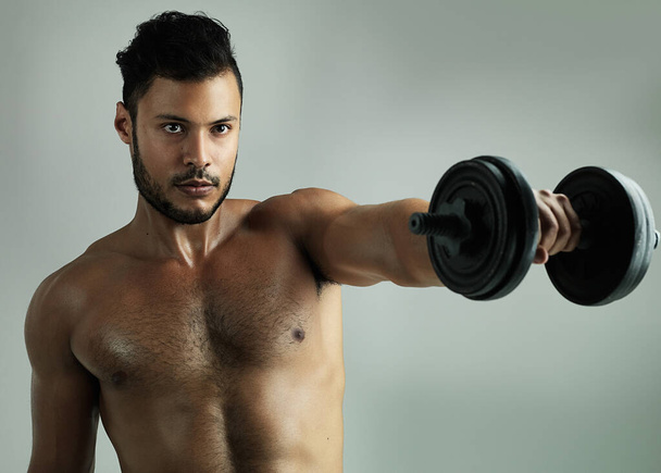 Hes ripping through those reps. Studio shot of a young man working out with a dumbbell against a gray background - Photo, Image