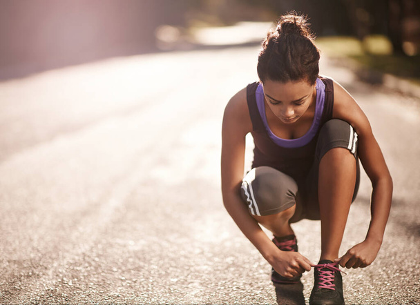 The only way to finish is to start. a runner tying her shoelaces before a run - Foto, imagen