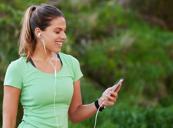 Getting into the zone with her favorite music. a young woman listening to music while out running - Foto, Bild