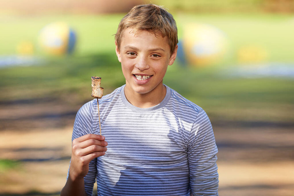 Mmm melted marshmallows. Portrait of a young boy holding a roasted marshmallow - Photo, image