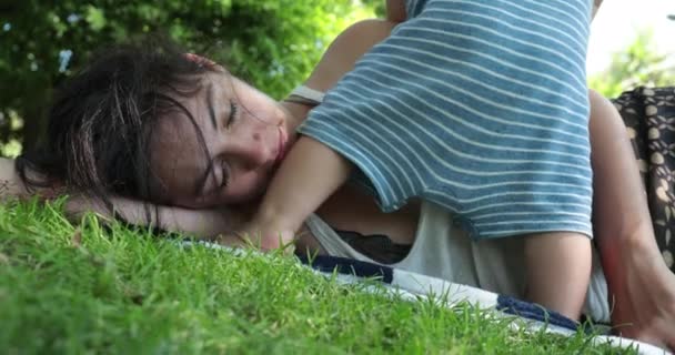Fáradt anya alszik a szabadban feküdt a füvön, a baba figyelmet akar, felébred a szülő szundikál - Felvétel, videó