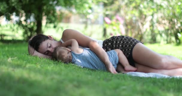 Μητέρα και μωρό ξαπλωμένοι στο γρασίδι μαζί ξεκουράζονται. Γονέας και βρέφος candid σπάσει - Πλάνα, βίντεο