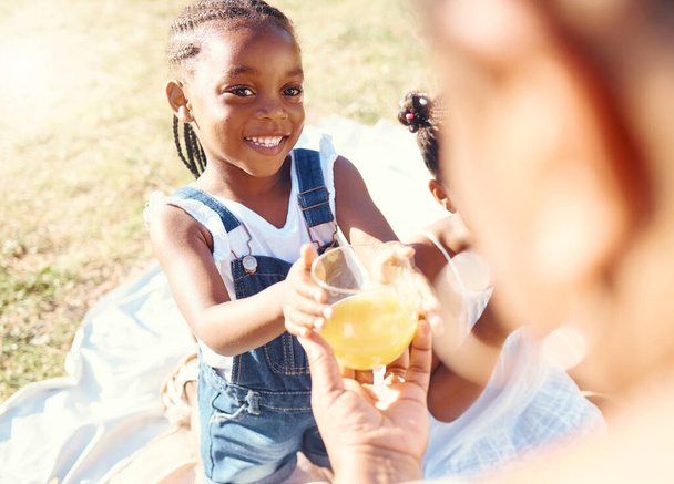 Happy girl, juice and smile in family picnic fun and joy in happiness on a warm summer day in nature. Black child smiling for fresh cold healthy beverage in the hot outdoors with parent and sibling. - Foto, Bild